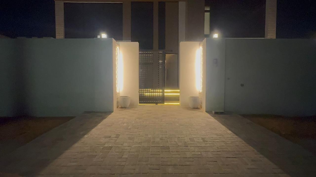 Lit entry passage running between high walls towards the house after dark.